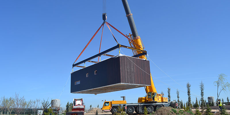 Prefabricated-Modular-Units-The-Future-of-Modern-Construction A large yellow crane is lifting a modular prefabricated home kept in an empty ground.